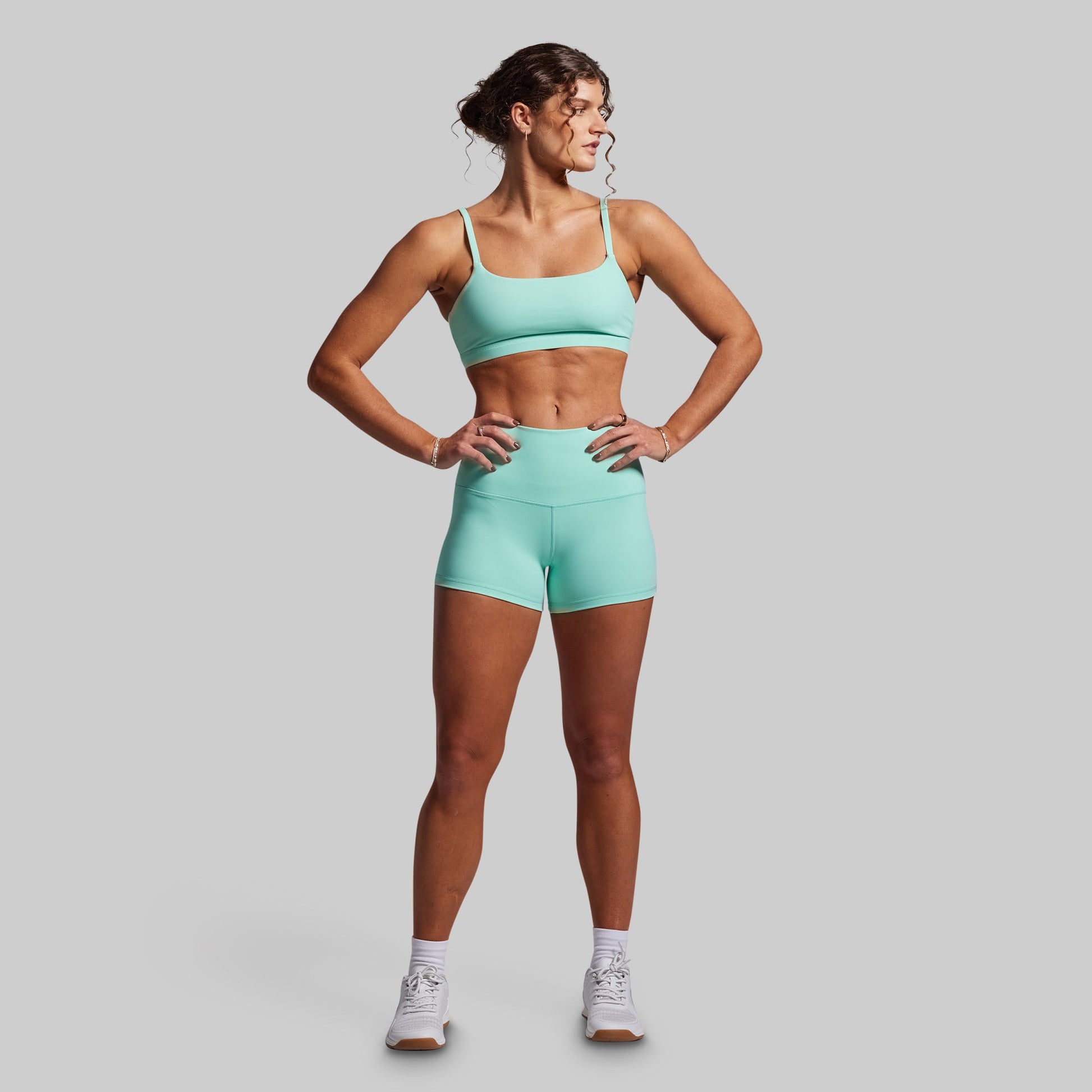 Woman wearing a teal sports bra and shorts set on a gray background