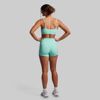 Person wearing a teal sports bra and shorts set on a gray background