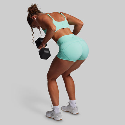 Woman in teal athletic wear lifting a dumbbell on a plain background