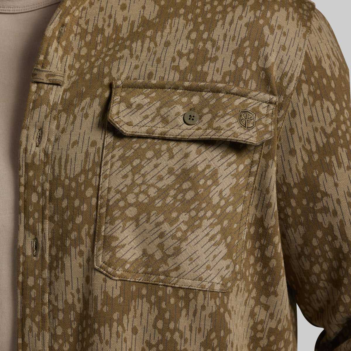 Close-up of a patterned button-up shirt with a chest pocket, featuring a tan and brown abstract brushstroke design.