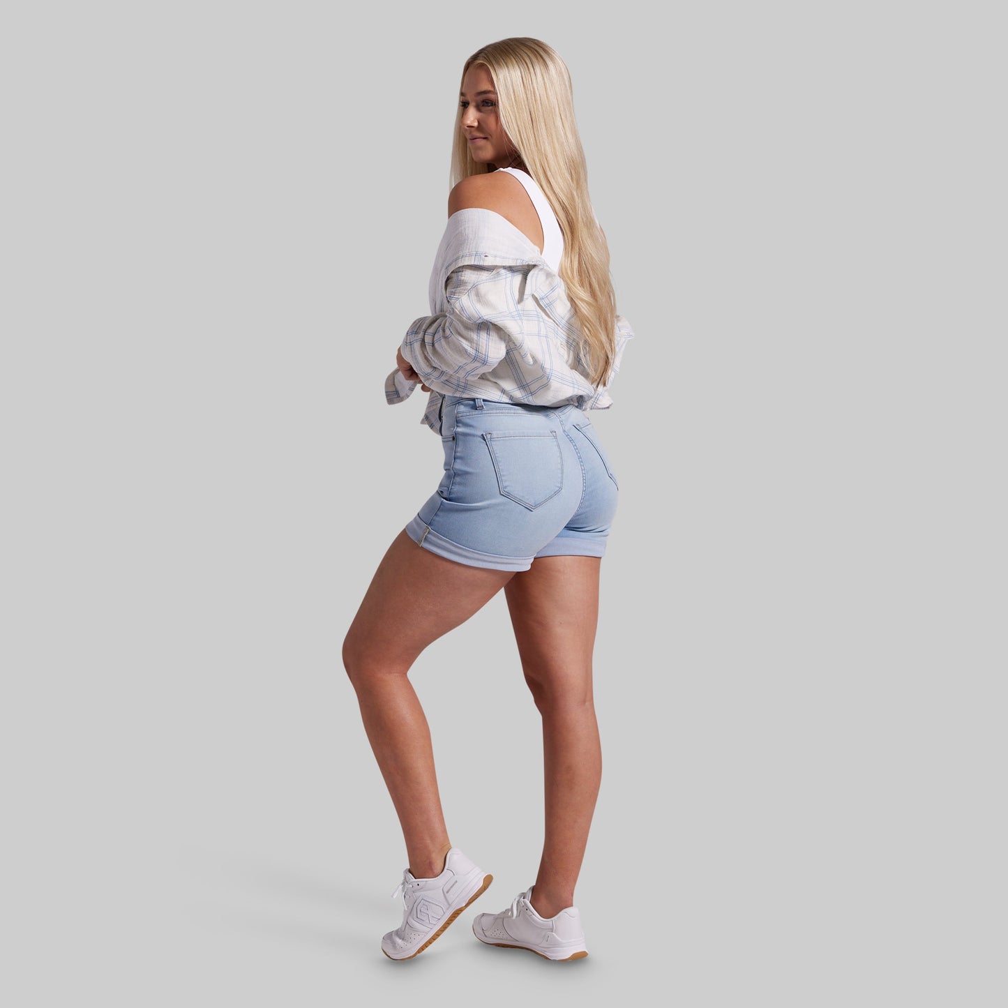 Woman wearing light blue denim shorts and a white off-shoulder top on a gray background