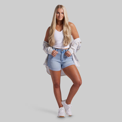 Woman wearing a white crop top, denim shorts, and white sneakers on a gray background