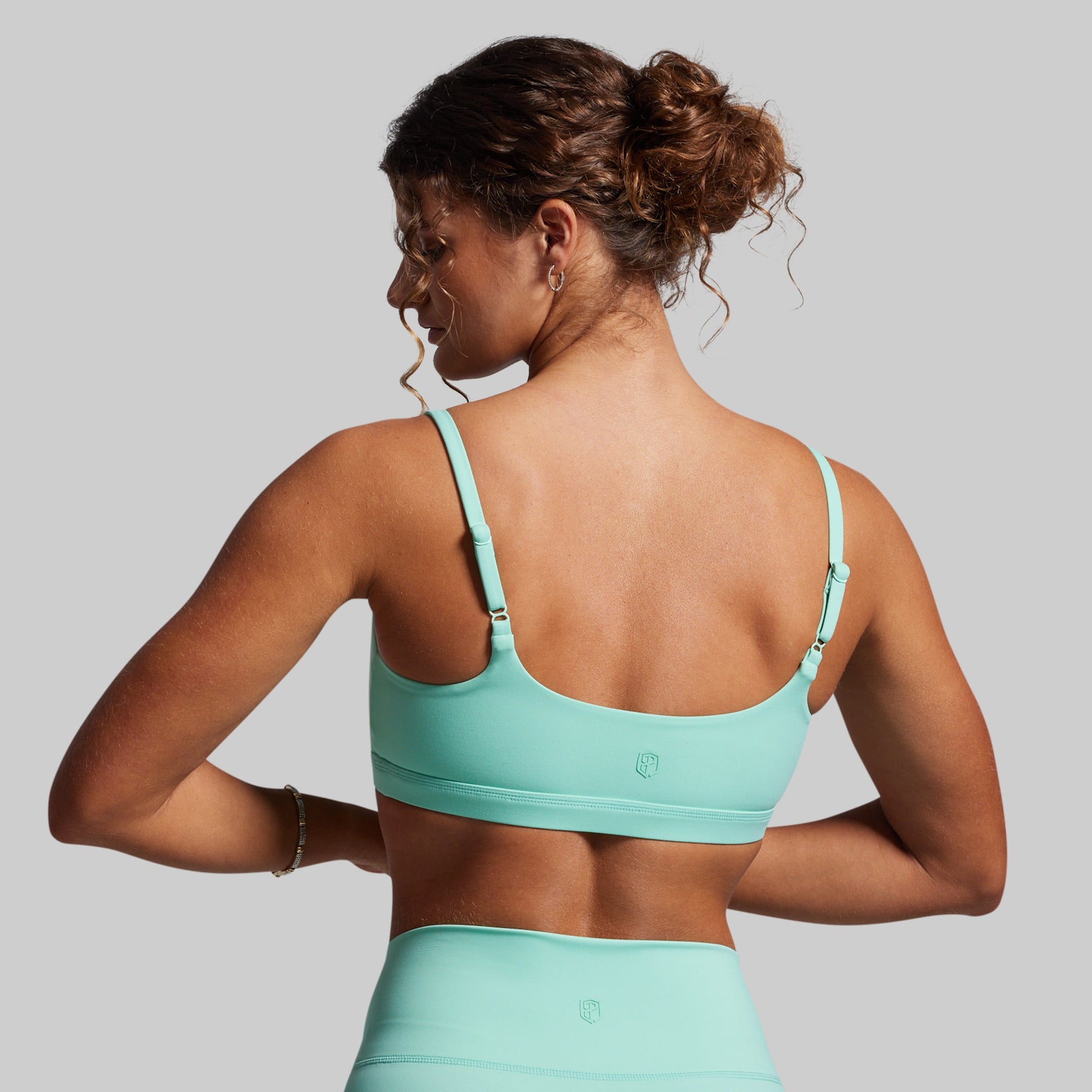 Woman wearing a teal sports bra against a gray background