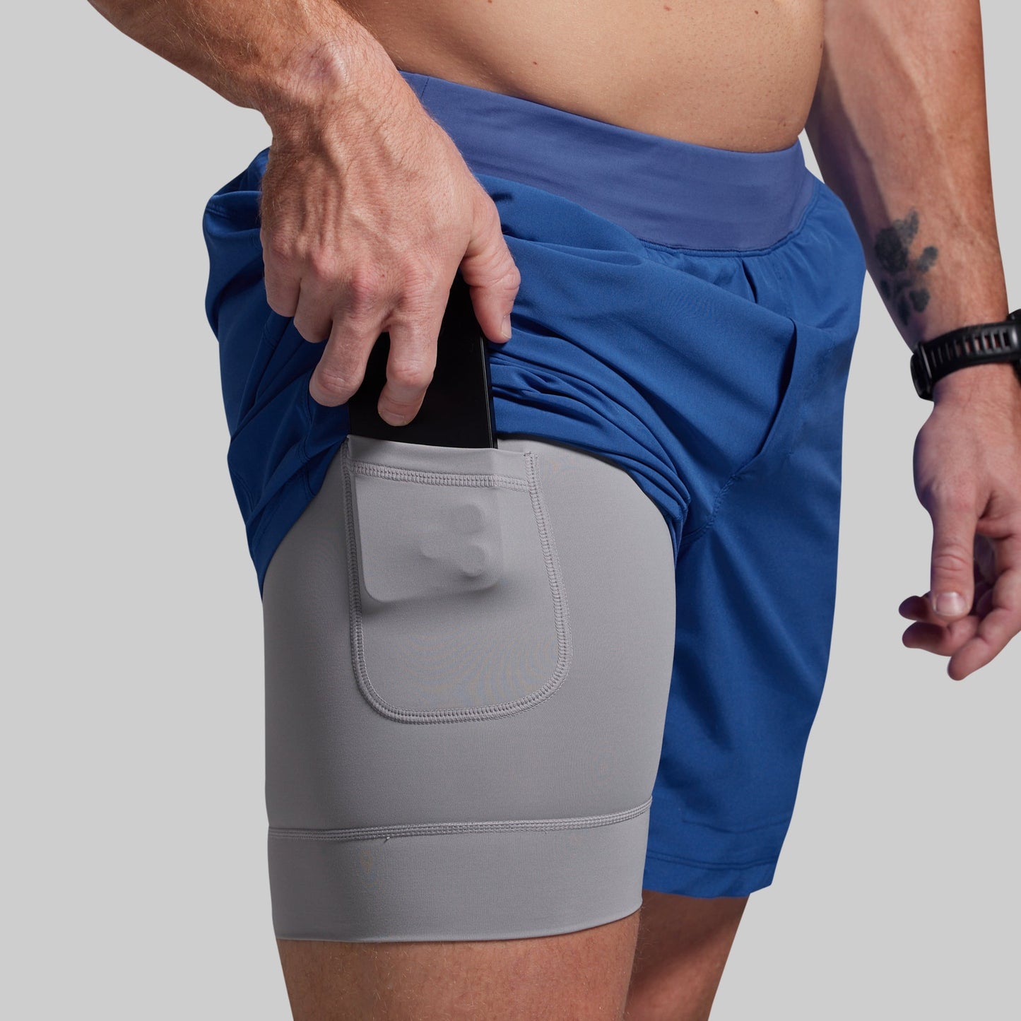 Two-tone shorts with a gray panel and blue top worn by a person on a light gray background