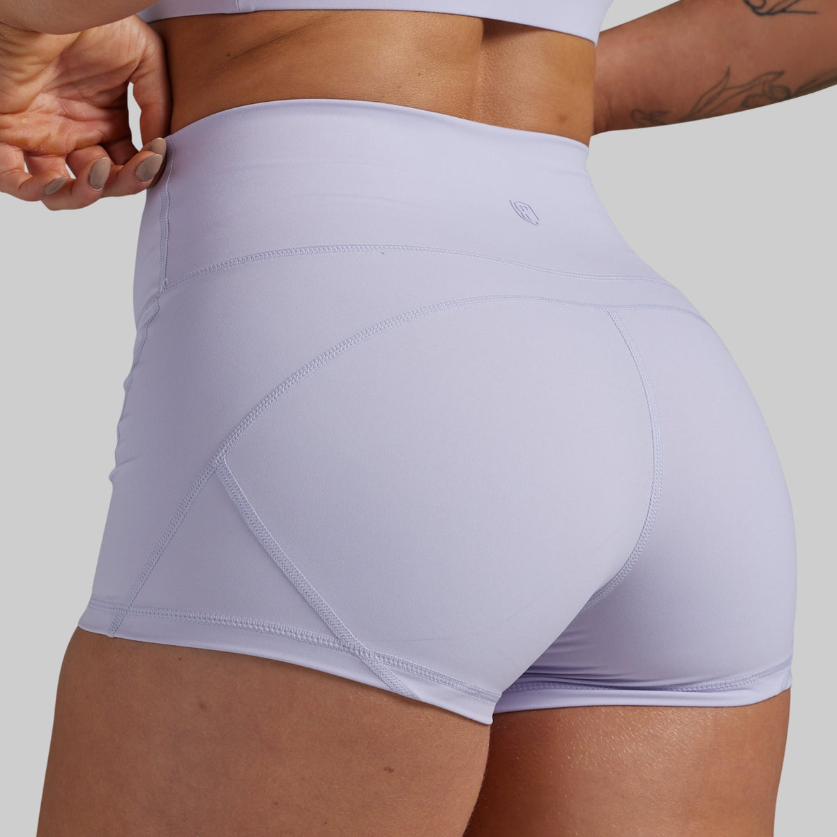 Close-up back view of a model wearing high-waisted light lavender athletic shorts with seam detailing, set against a solid gray background.