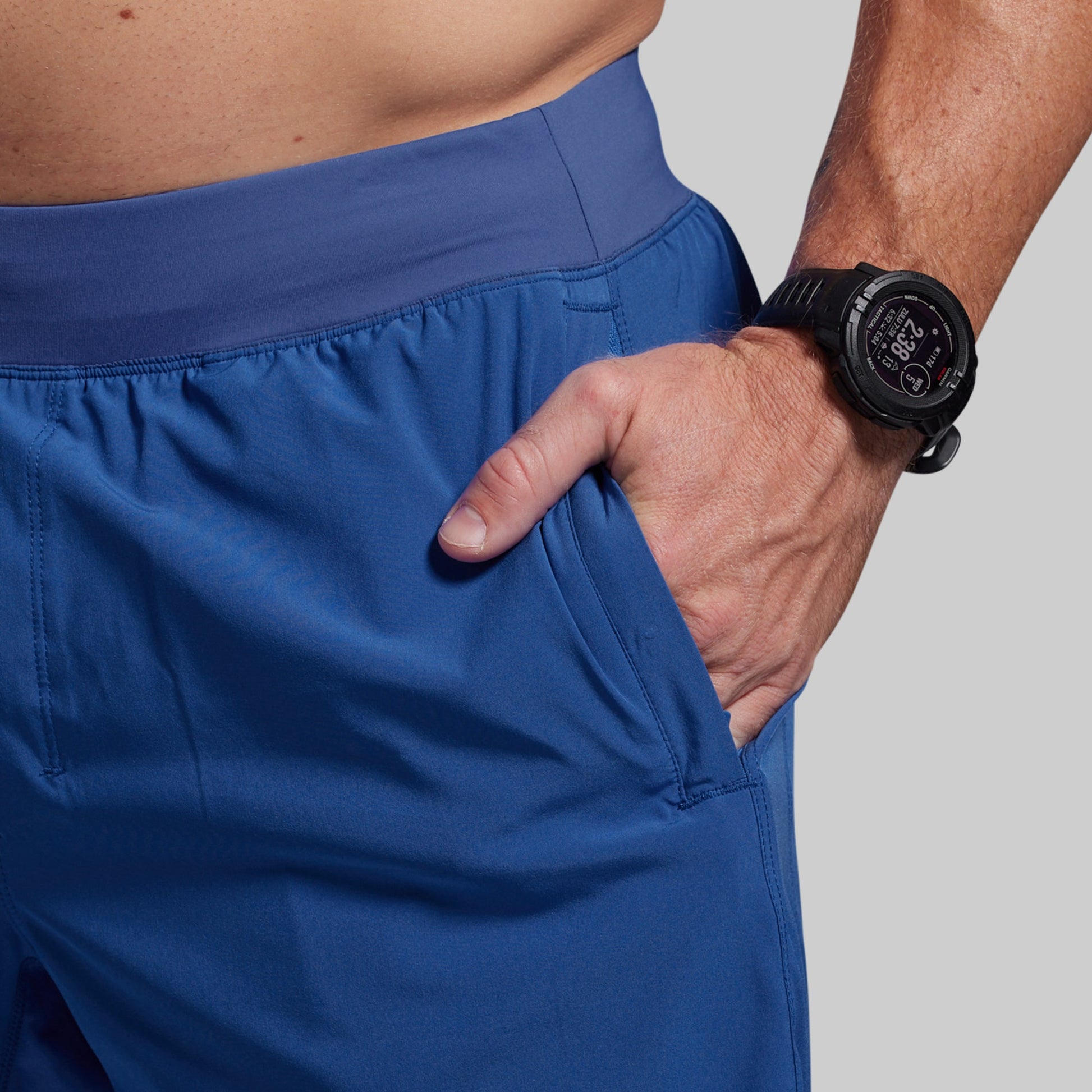 Person wearing blue shorts with a hand in one pocket, wearing a black smartwatch on the wrist.