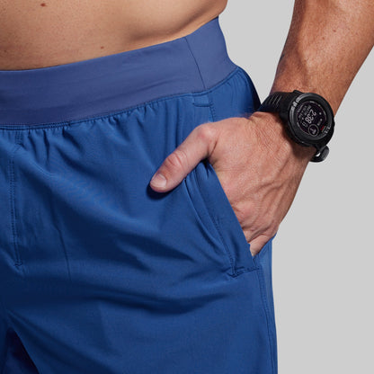 Person wearing blue shorts with a hand in one pocket, wearing a black smartwatch on the wrist.