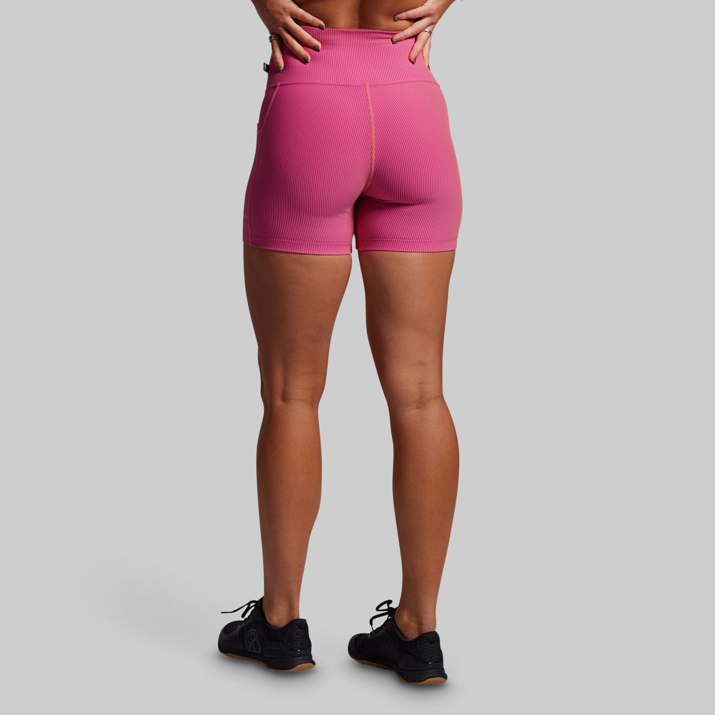 Person wearing pink ribbed athletic shorts on a gray background