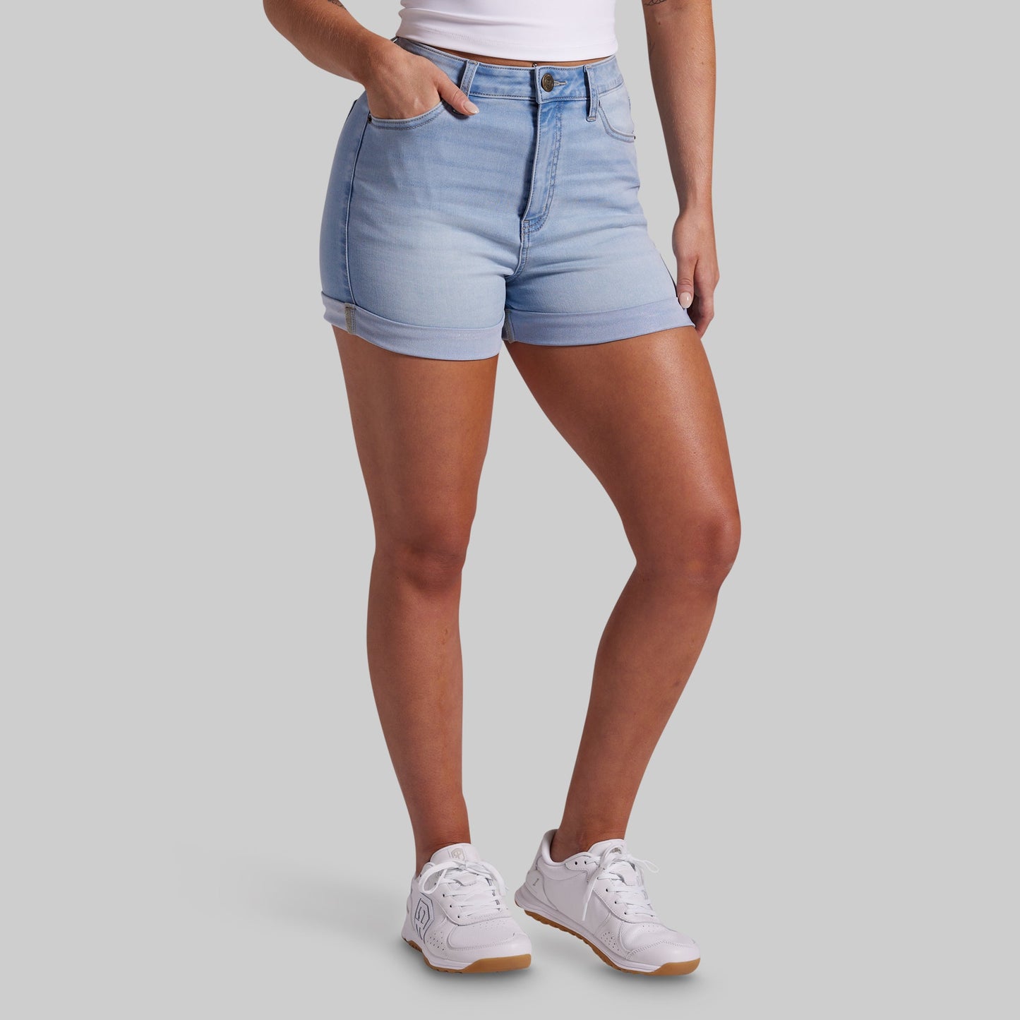 Person wearing light blue denim shorts and white sneakers on a plain background