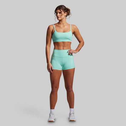 Woman wearing a matching teal sports bra and shorts set on a gray background
