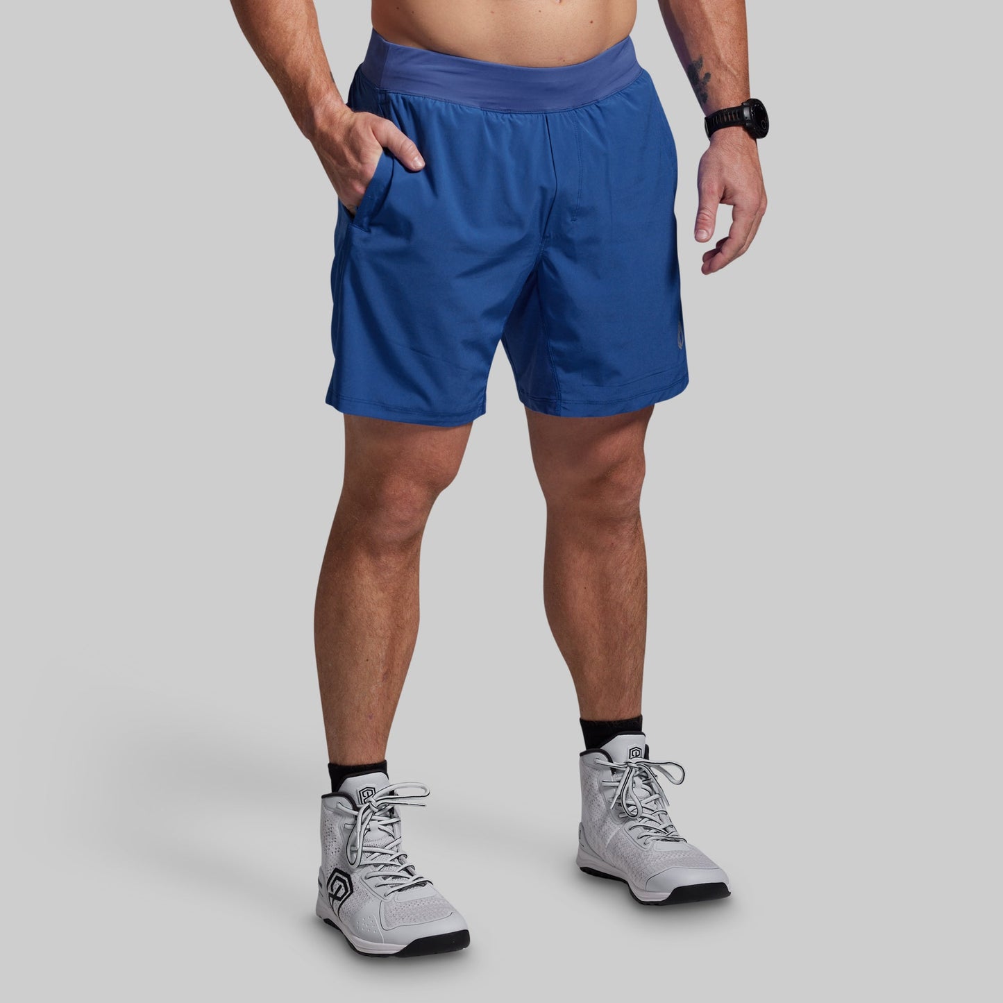 Person wearing blue athletic shorts and white sneakers on a gray background