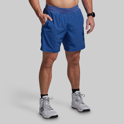 Person wearing blue athletic shorts and white sneakers on a gray background