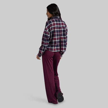 A woman shown from the back wearing a dark red, navy, and white plaid flannel shirt and matching dark burgundy pants, standing against a solid light gray background.