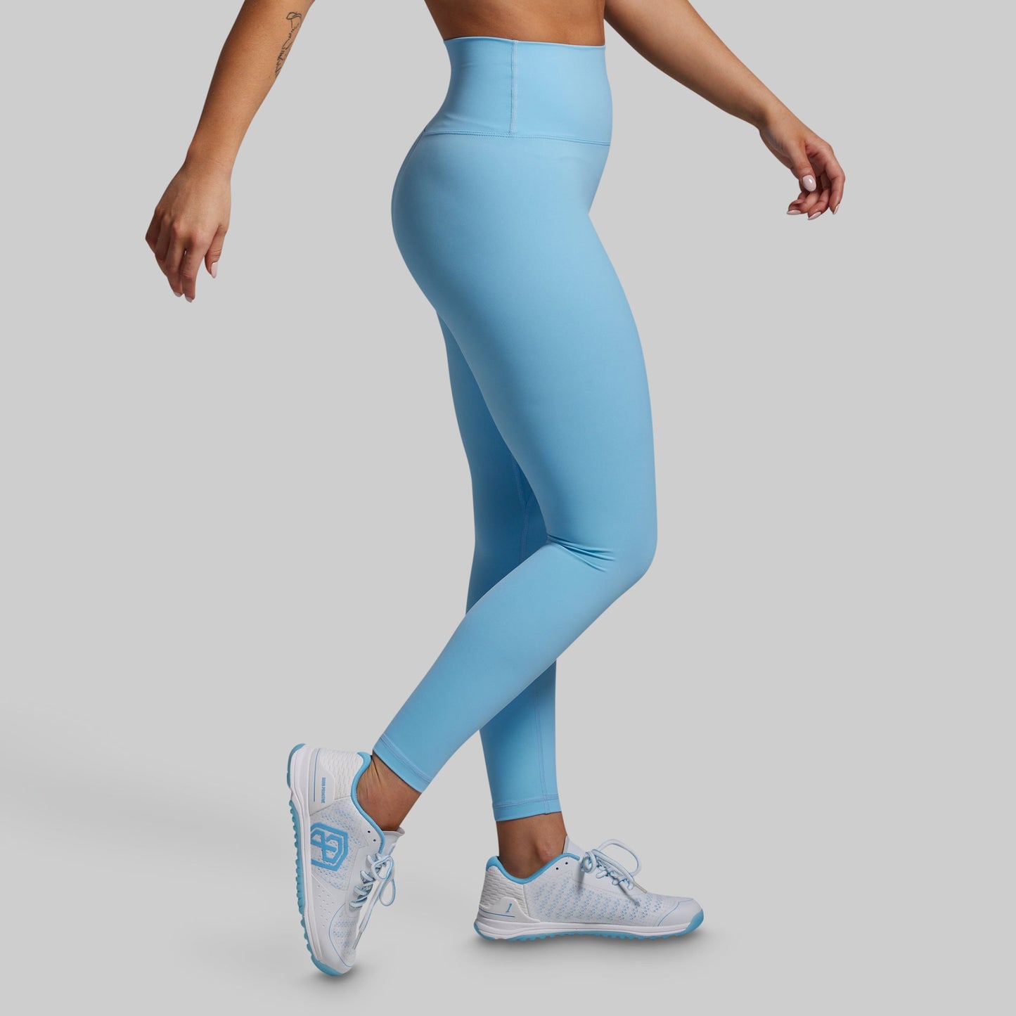 Person wearing light blue leggings and white sneakers on a gray background
