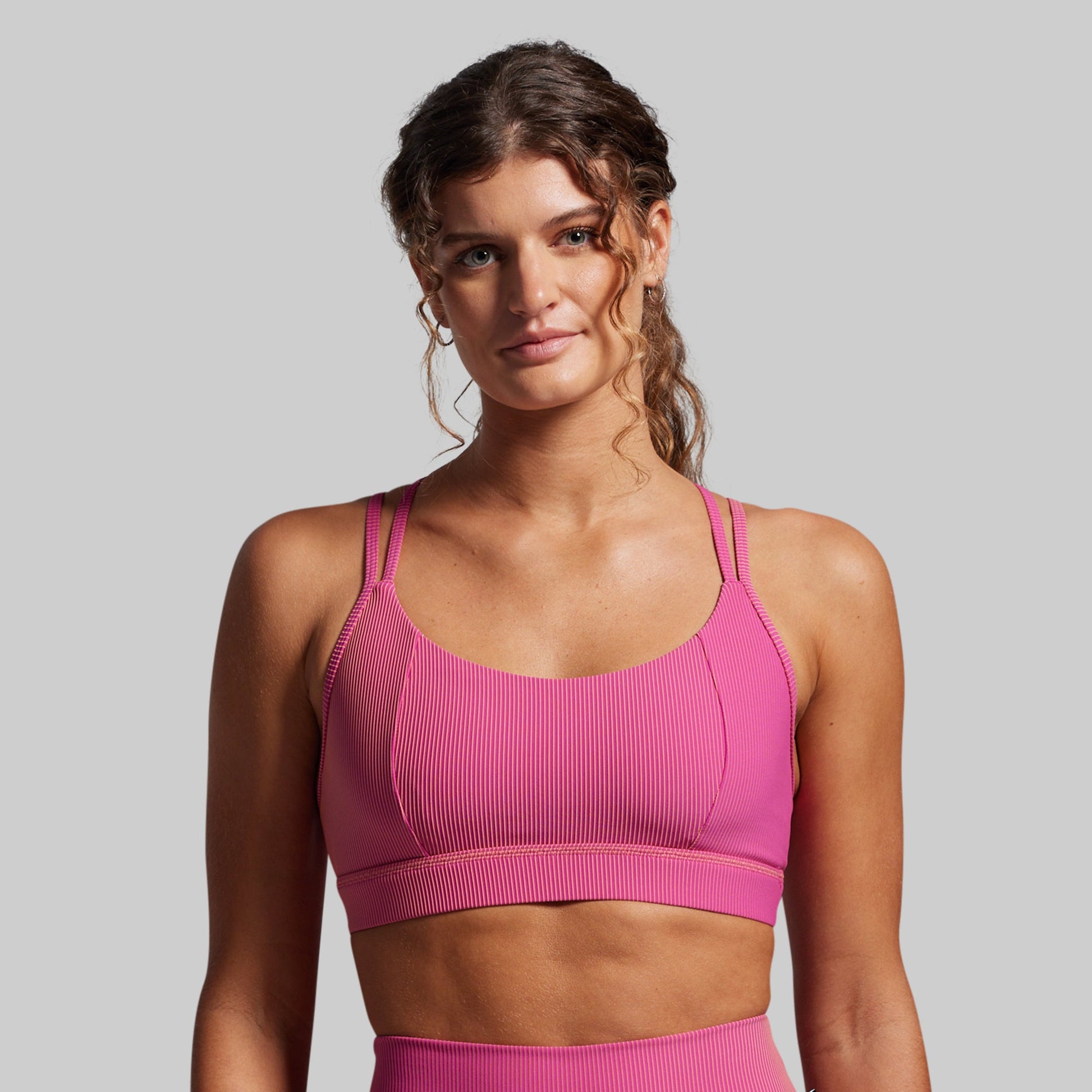 Woman wearing a pink ribbed sports bra and leggings against a gray background