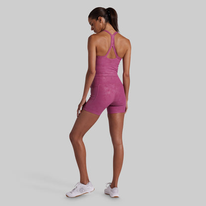 A woman modeling a pink athletic matching set from the back, standing against a solid light gray background.