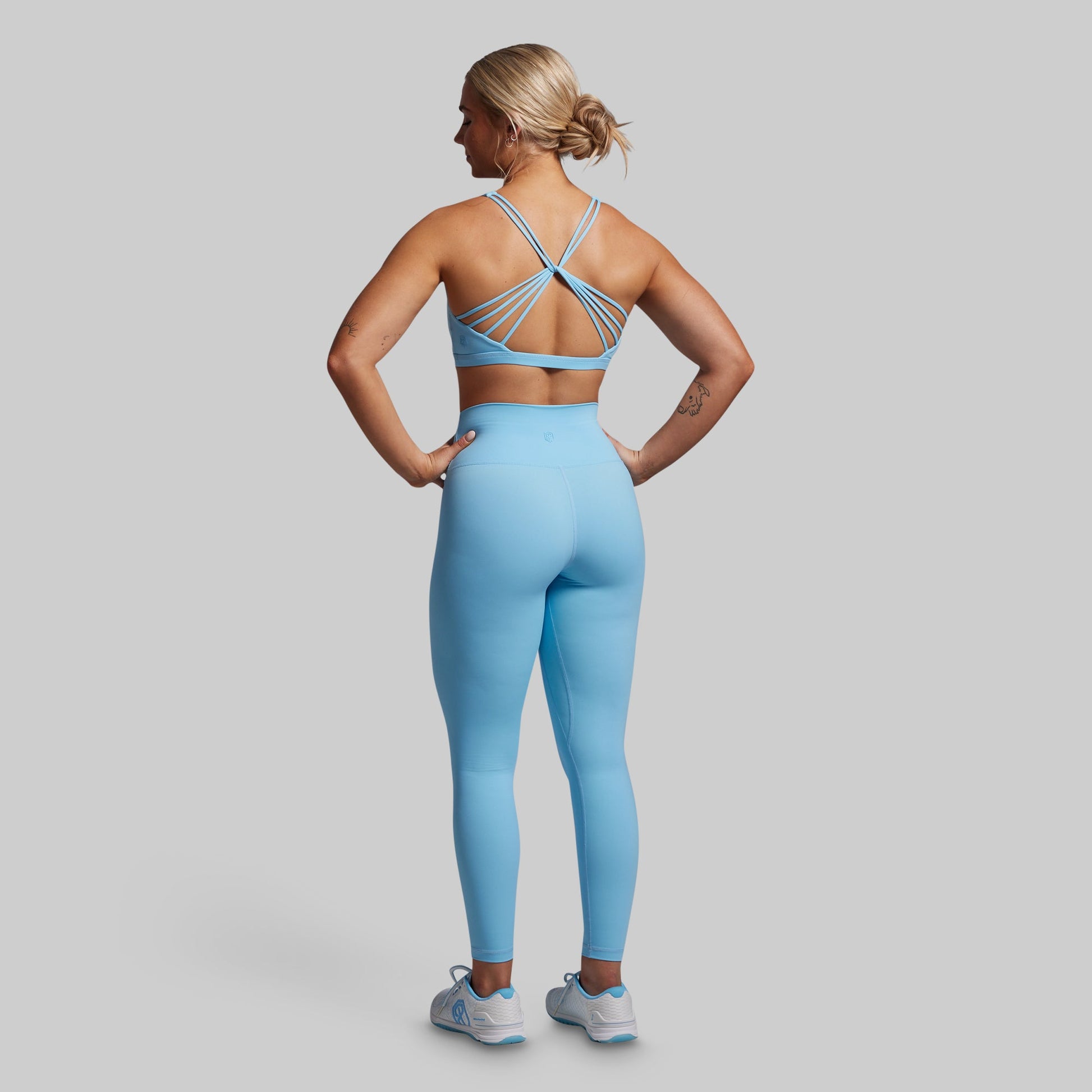 Woman wearing a blue sports bra and leggings set on a gray background