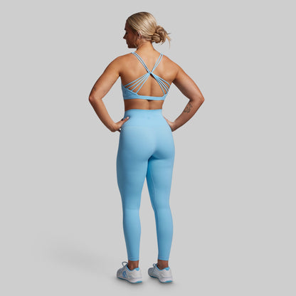Woman wearing a blue sports bra and leggings set on a gray background