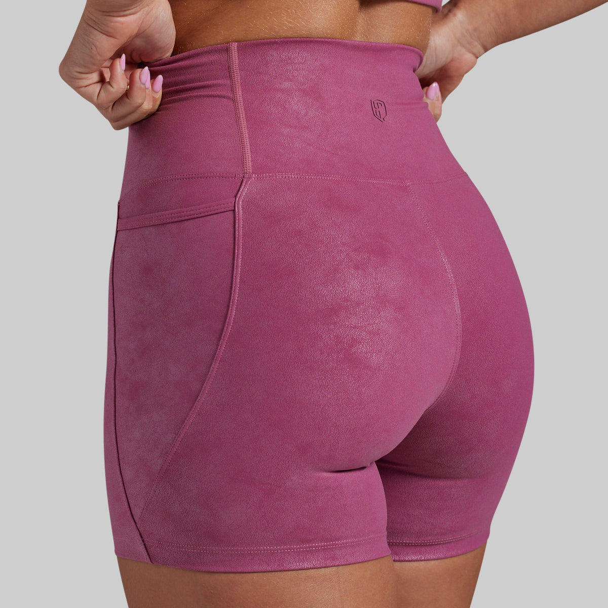Rear view of a person wearing high-waisted athletic shorts in a dusty rose pink color, showing the pockets and waistband details against a solid gray background.