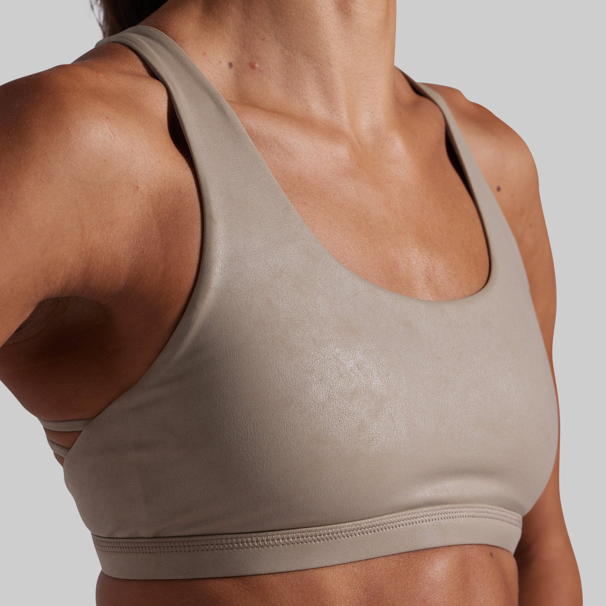 Close-up of a woman wearing a seamless athletic sports bra in a light taupe-beige color, showing the molded cup and underband against a solid gray background.