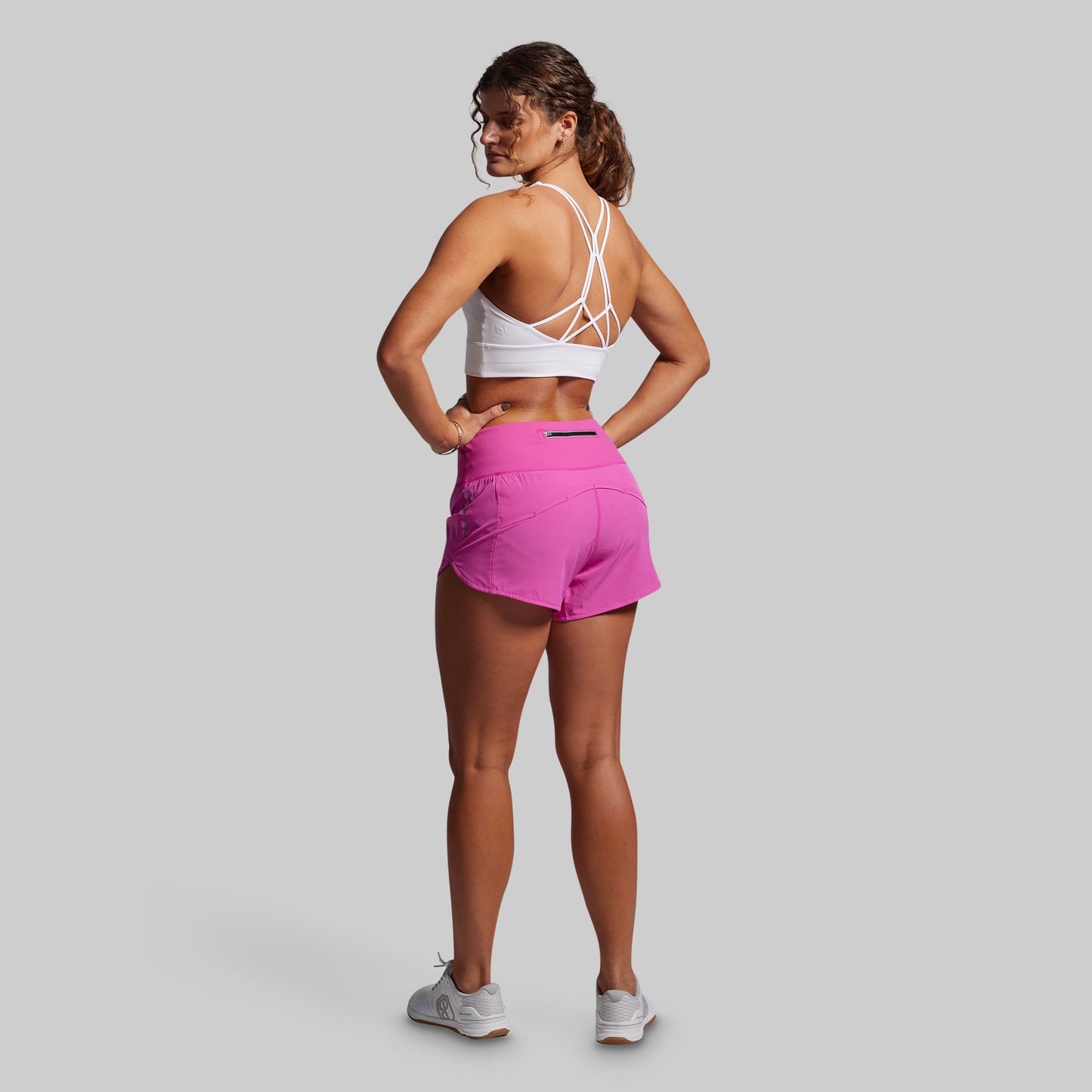 Woman wearing a white sports bra and pink shorts on a gray background