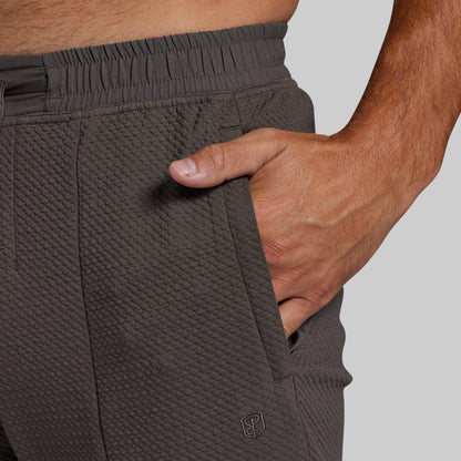 Close-up of a person wearing textured dark gray athletic joggers, showing the side pocket with a hand inserted and an elastic waistband.