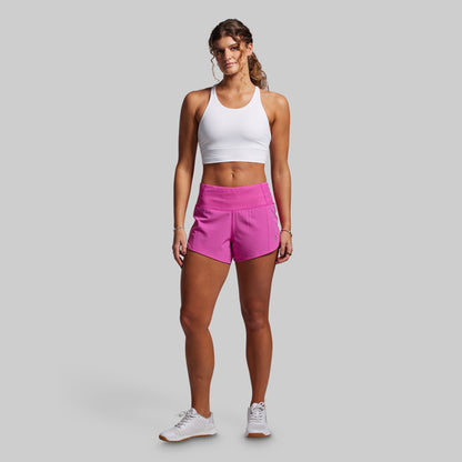 Woman wearing a white tank top and pink shorts on a gray background