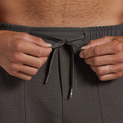 Close-up of a person wearing textured dark gray athletic joggers, pulling the drawstring at the elastic waistband.