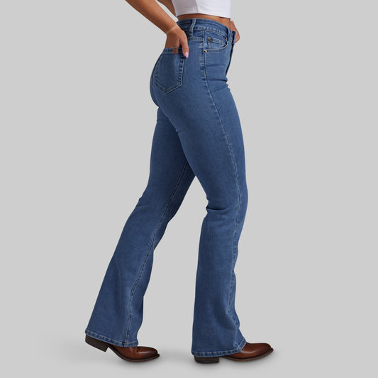 A model wearing a pair of medium-wash blue bootcut jeans, shown from the waist down in a side profile against a solid gray background.