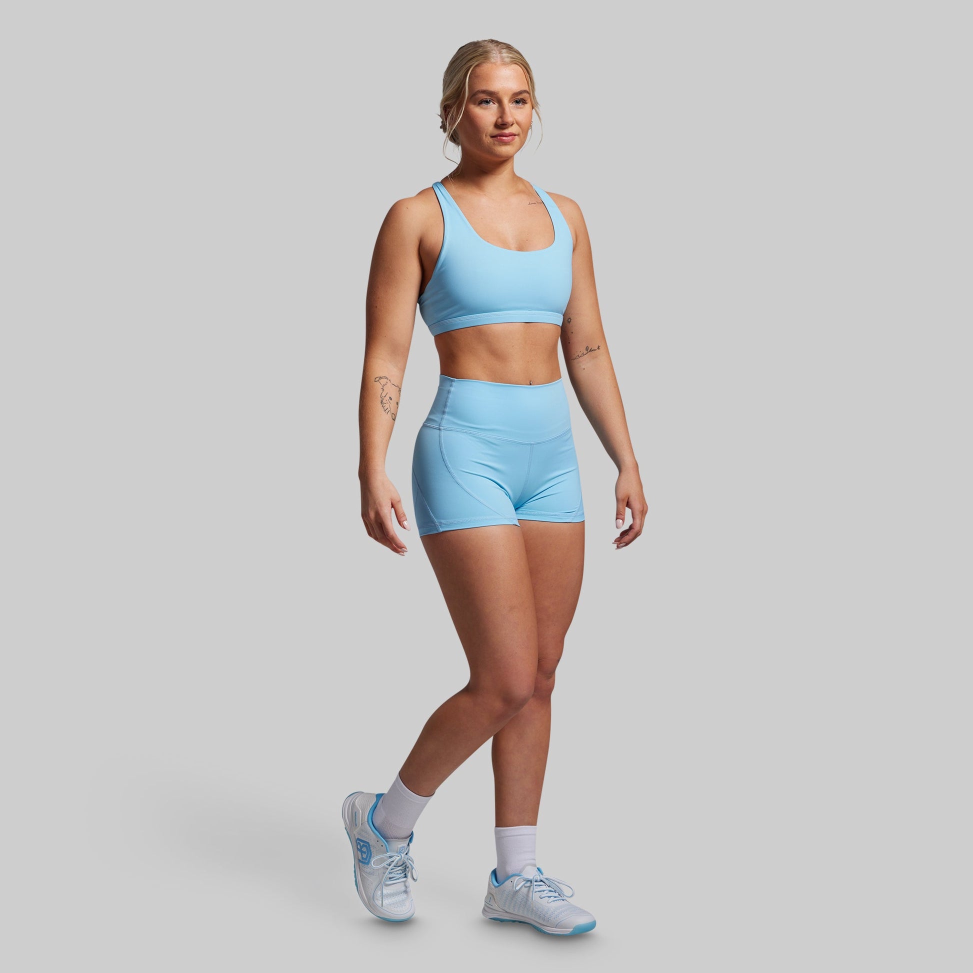 Woman wearing a light blue sports bra and shorts set on a gray background