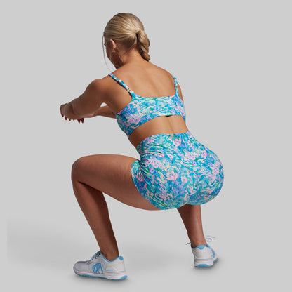 Woman wearing a colorful floral sports bra and shorts set on a plain background
