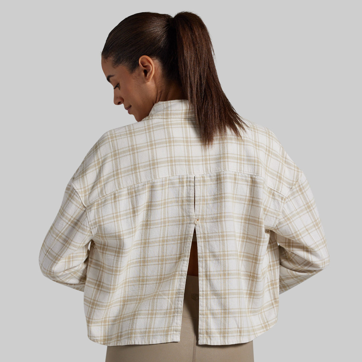 A woman shown from the back wearing a cropped, long-sleeve plaid shirt in beige and white, with a small center back slit.