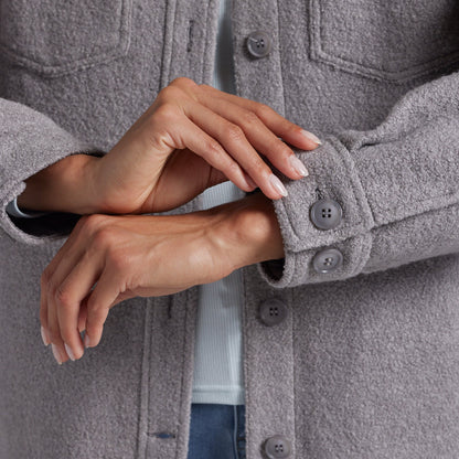 Close-up of a person wearing a textured gray button-front jacket, showing both hands and the cuff detail with matching gray buttons.