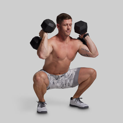 Man performing a squat exercise with dumbbells on a plain background