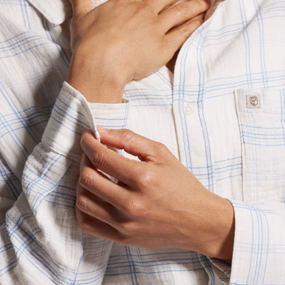 Close-up of a person wearing a light blue and white checkered shirt with hands adjusting the collar.