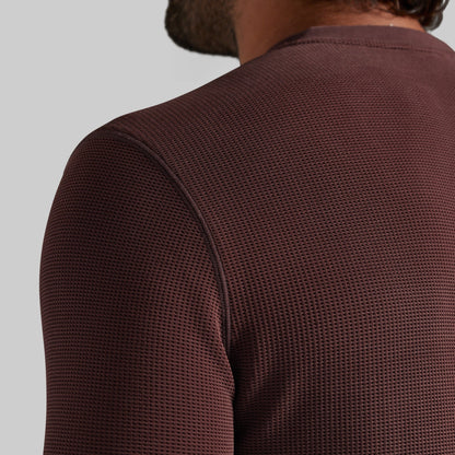 Close-up back view of a person wearing a textured, waffle-knit long-sleeve shirt in a deep burgundy brown color, set against a solid light gray background.