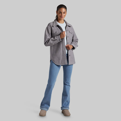 A woman modeling a heather gray button-up jacket over a white t-shirt and blue jeans, standing against a solid gray studio background.