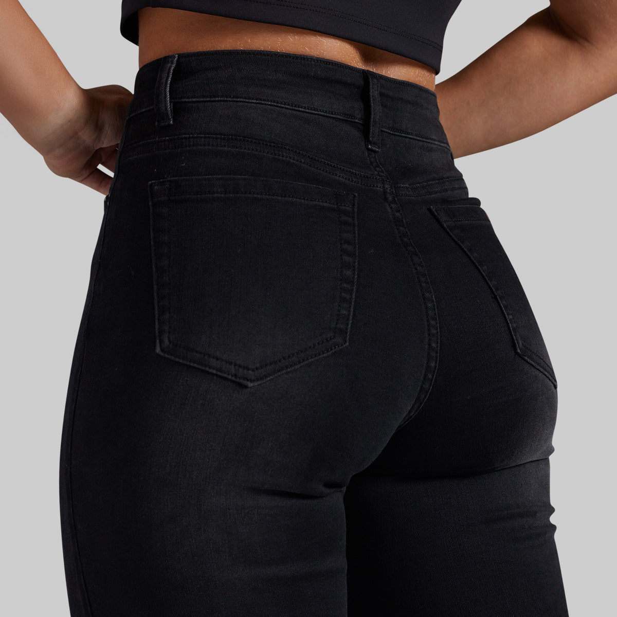 Close-up back view of a person wearing black high-waisted skinny jeans against a light gray studio background.