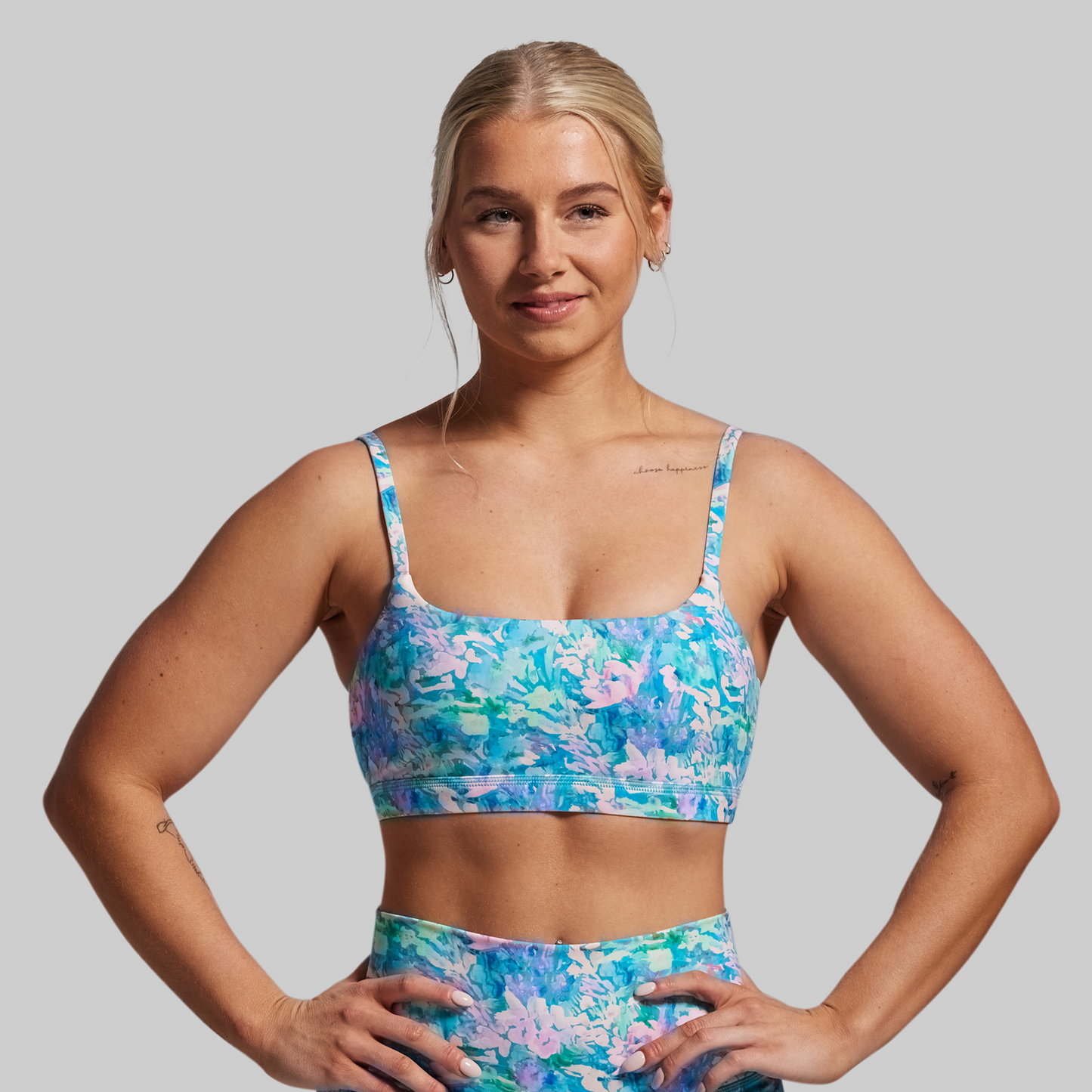 Woman wearing a colorful floral sports bra and shorts on a gray background