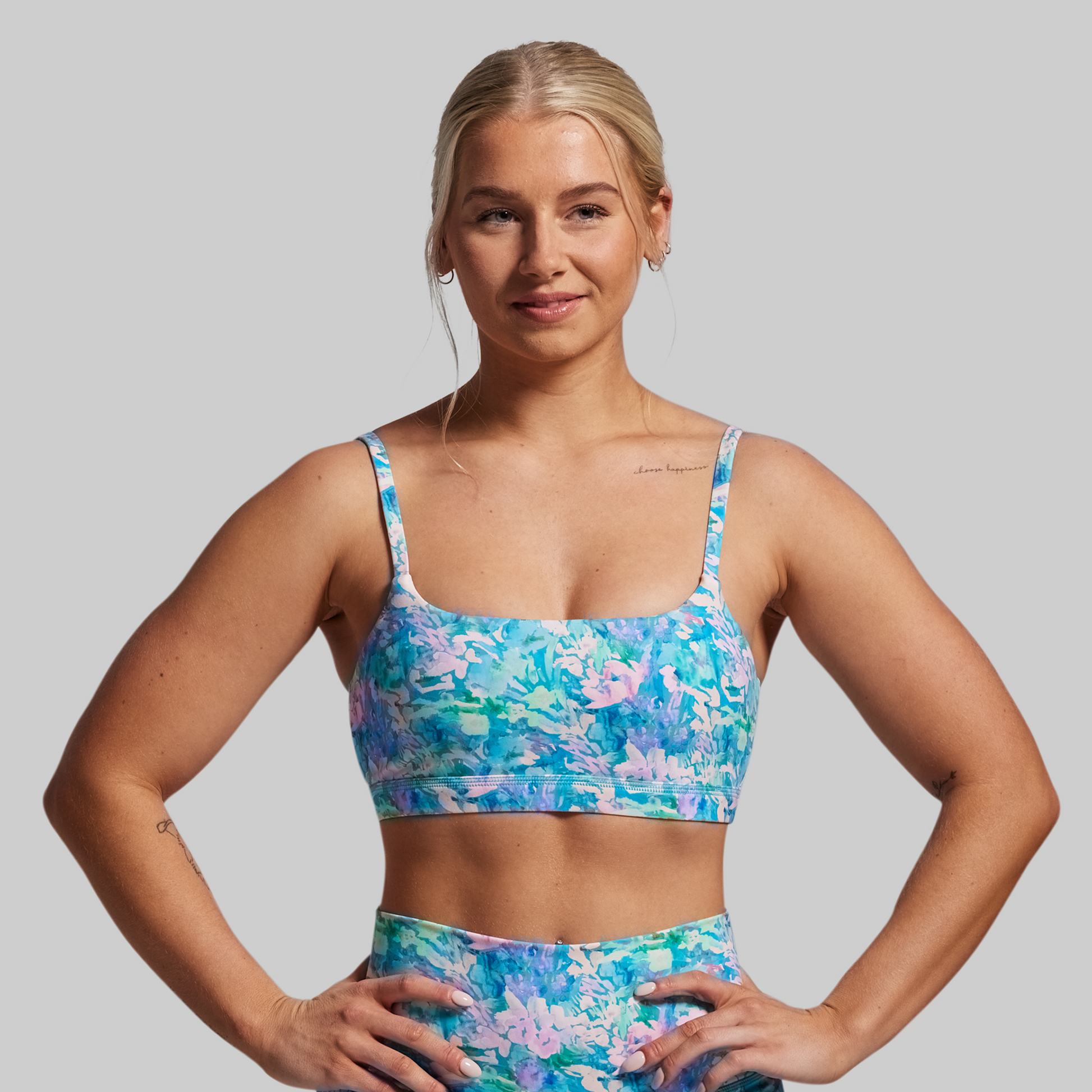 Woman wearing a colorful floral sports bra and shorts on a gray background