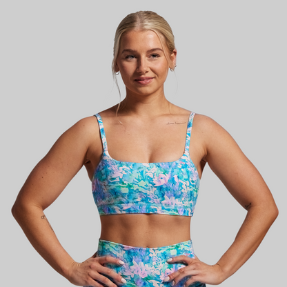 Woman wearing a colorful floral sports bra and shorts on a gray background