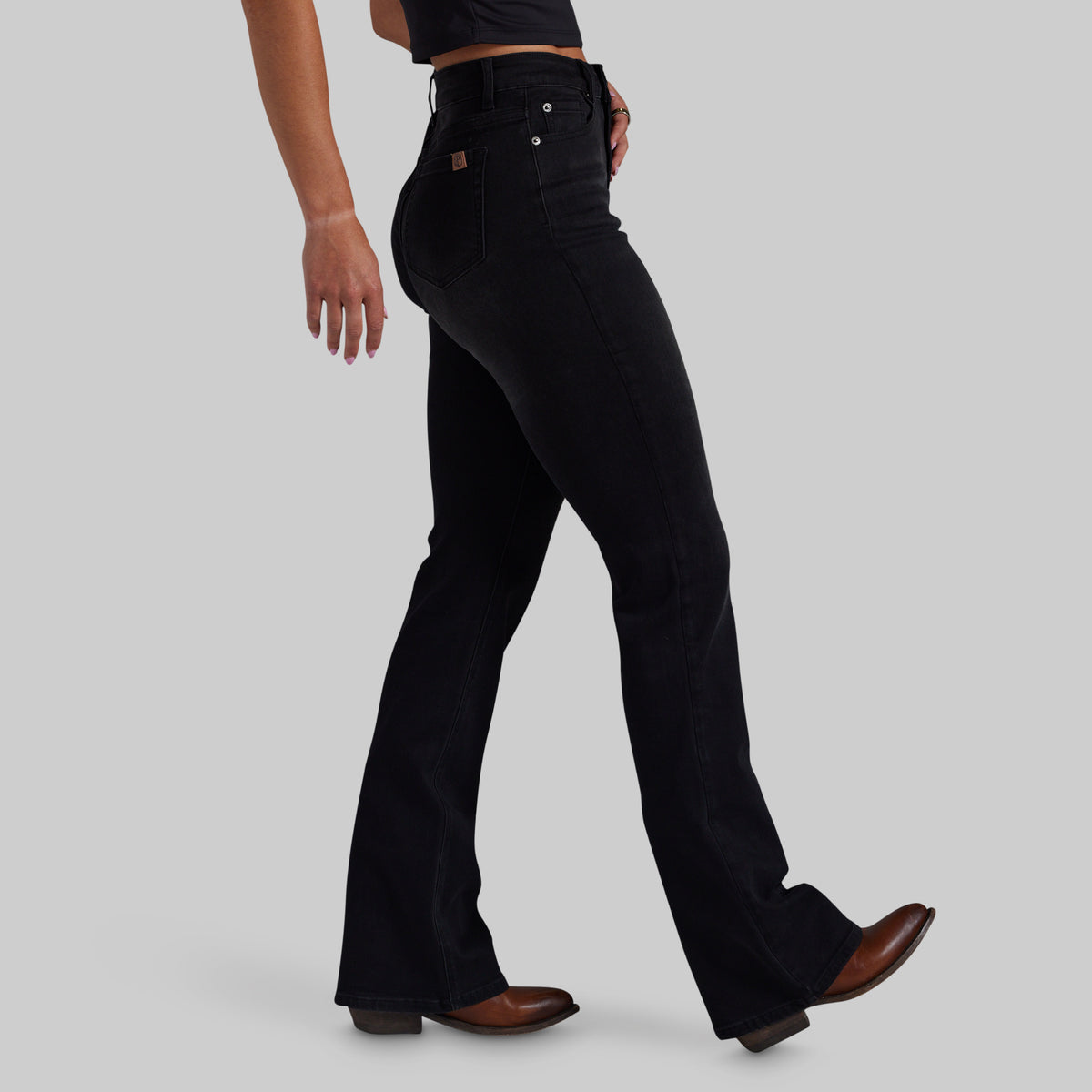 A model wearing a pair of black mid-rise bootcut jeans, shown from the waist down in a side profile against a solid gray background.