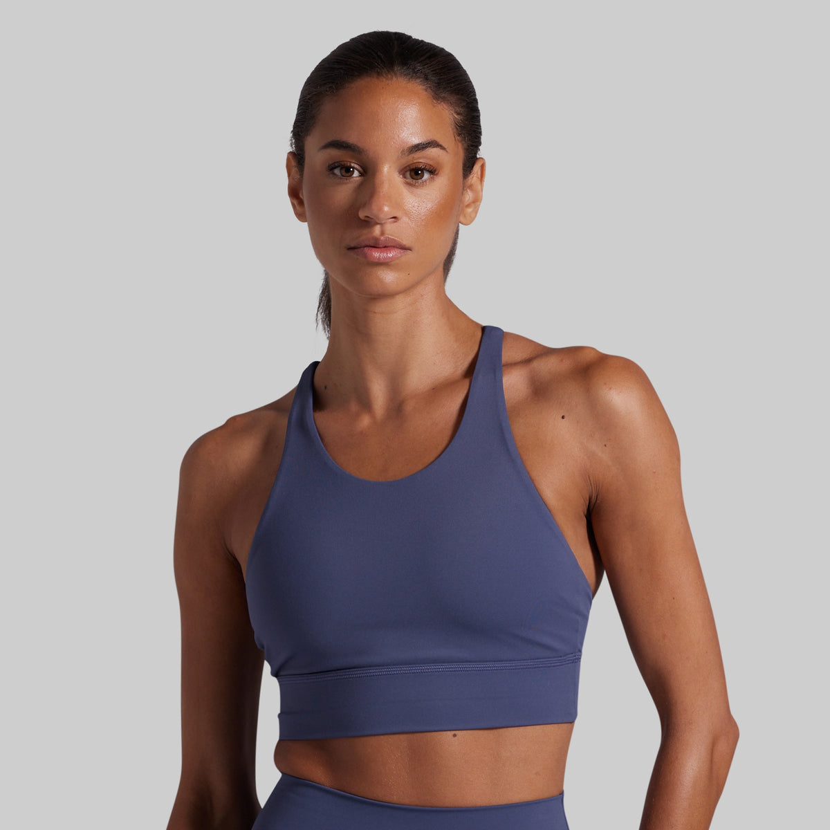 A woman modeling a slate blue athletic sports bra against a solid light gray background.