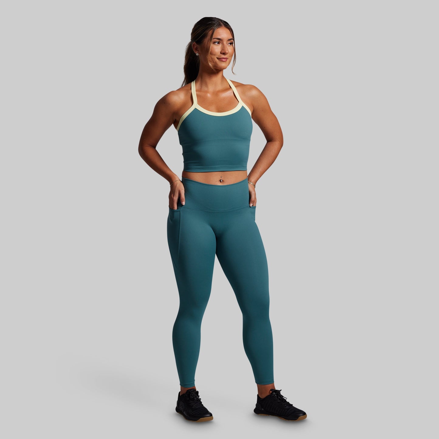 Woman wearing a teal sports bra and leggings set on a gray background