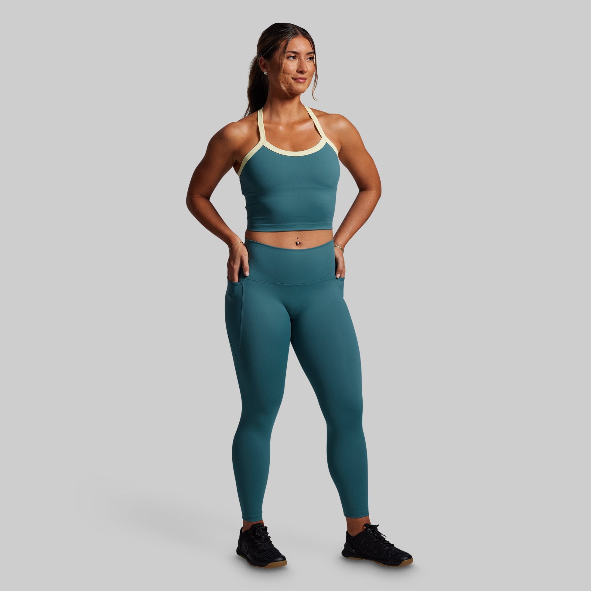 Woman wearing a teal sports bra and leggings set on a gray background
