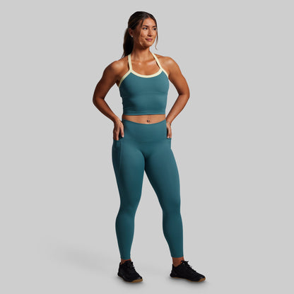 Woman wearing a teal sports bra and leggings set on a gray background