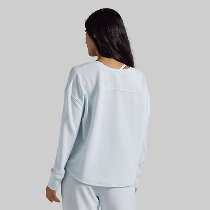 A woman shown from the back wearing a light blue long-sleeve athletic top and matching light blue pants against a solid gray studio background.