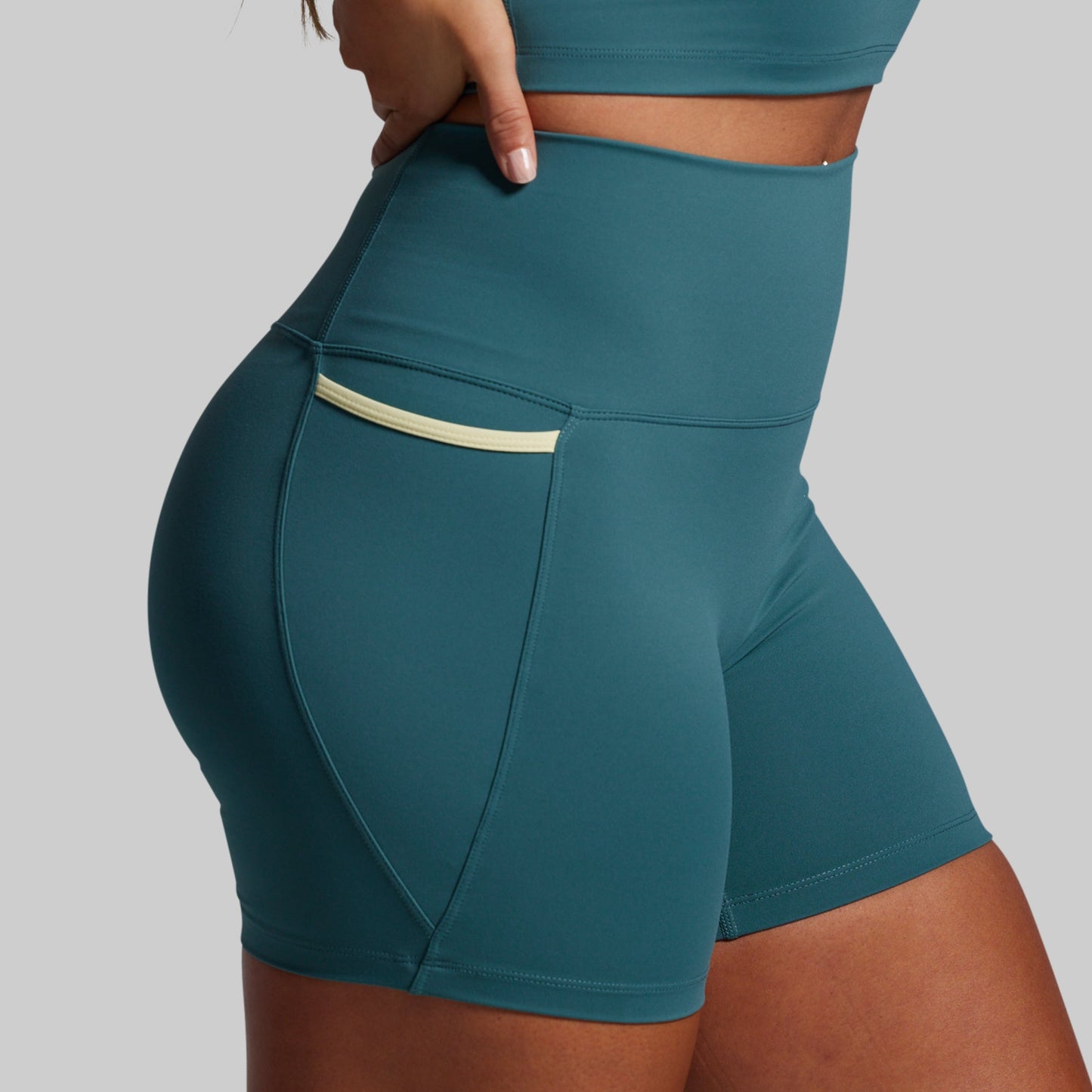Teal athletic shorts with a pocket on a gray background