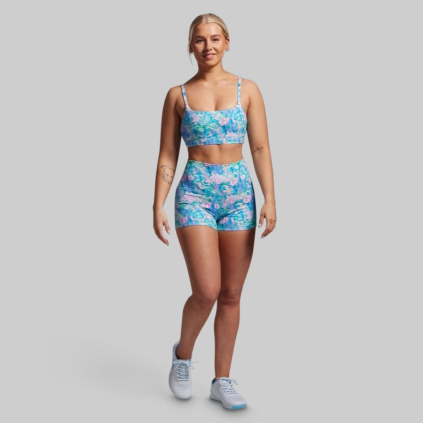 Woman wearing a blue floral sports bra and shorts set on a gray background