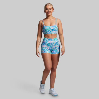 Woman wearing a blue floral sports bra and shorts set on a gray background